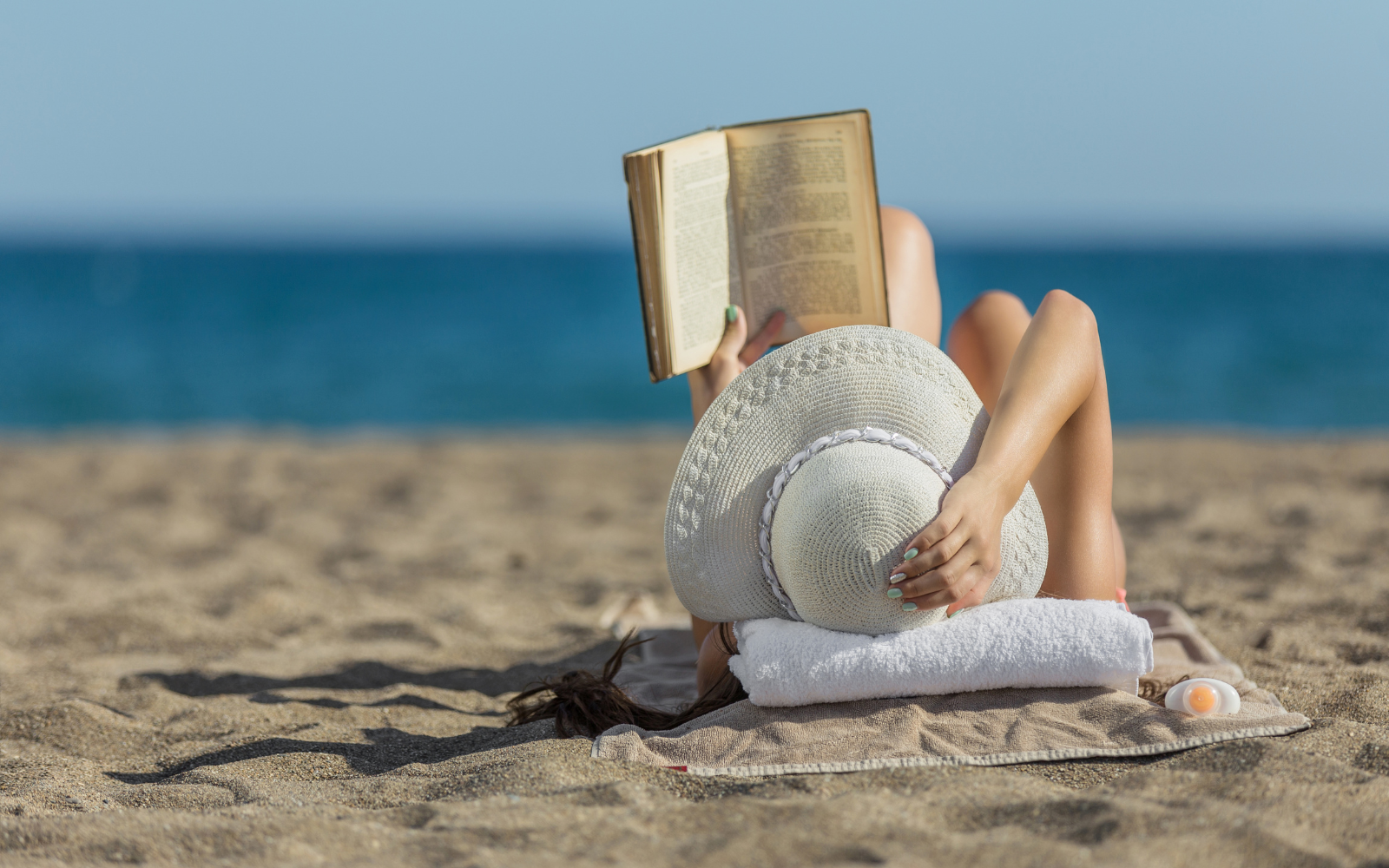 Pessoa lendo um livro na praia com o mar ao fundo