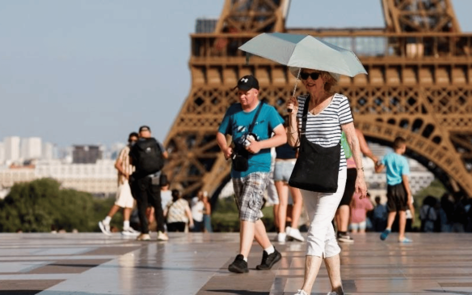 Viajantes caminhando sob sol forte diante da Torre Eiffel